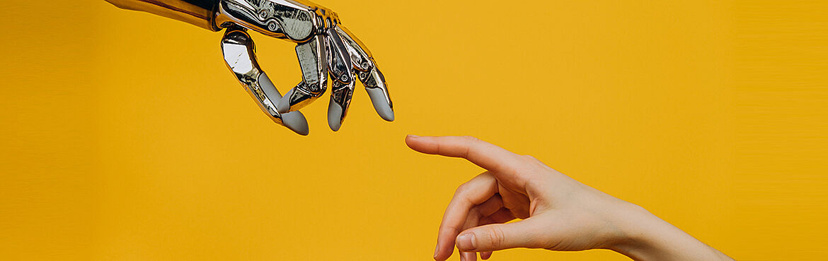 Robotic arm and a woman's hand pull their fingers together on a yellow background